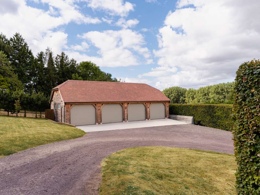 Large four-bay oak framed barn-style garage with clay plain tile roof and larch cladding at the end of a gravel drive near Tarrant Gunville, Dorset, designed and built by Dorset Timber Framing