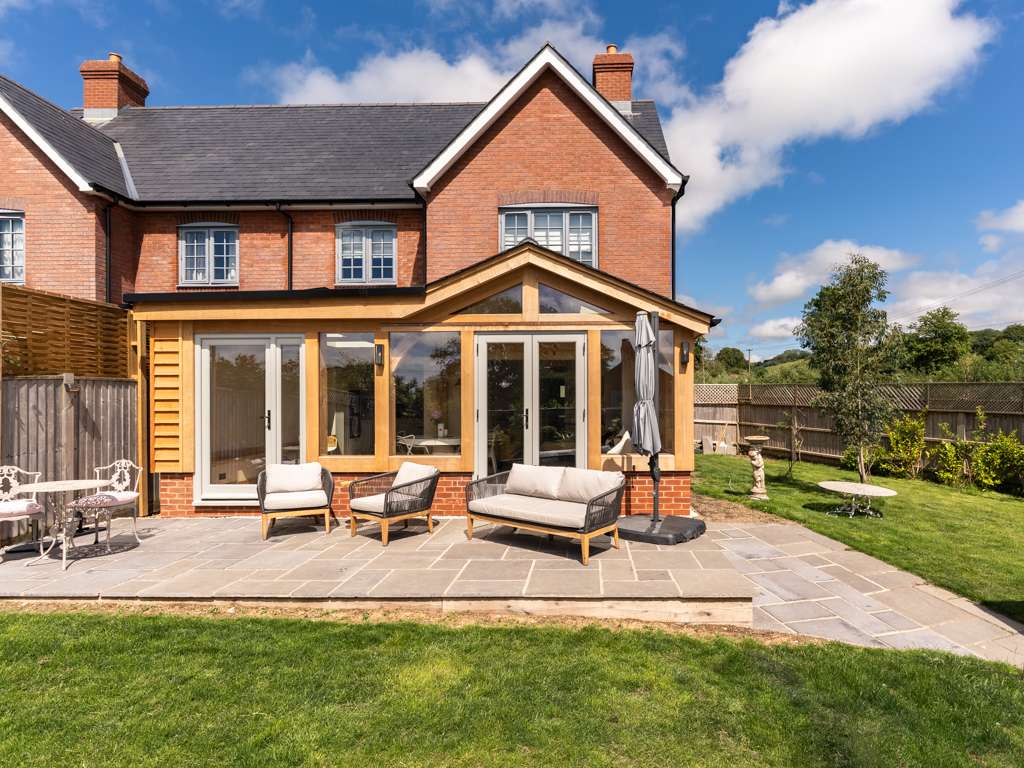 Oak framed garden room extension on the back of a new build brick home, with Spanish slate roof, Accoya doors and stone patio in Fontmell Magna, Dorset, designed and built by Dorset Timber Framing