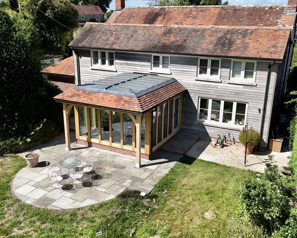 Aerial view of a new oak framed piano room extension with lead roof, clay plain tile hips, full-height direct glazing and stone patio, near Tisbury, Wiltshire